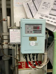 Technician calibrating a Fellow Kogyo FOCAS-1800 oil content meter on board a vessel beside an oily water separator panel with toolbox and certificate forms visible.