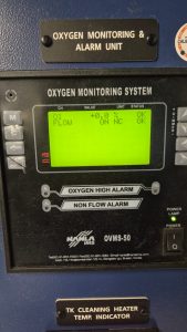 Hanla IMS OVMS-50 oxygen monitoring and alarm unit onboard a tanker, displaying oxygen level and flow status during calibration and functional testing service in Spain, including Algeciras, Gibraltar, Huelva, Cartagena, Barcelona, and Bilbao.