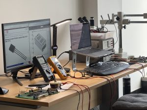 Marine electronics repair bench with test instruments, multimeters, laptop, and PCB controller under diagnostic and reconditioning work.