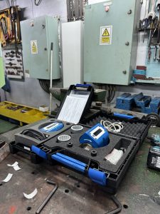 Torque wrench calibration kit laid out on a workshop bench on board a ship, showing digital torque instruments in a protective case with marine electrical panels in the background.